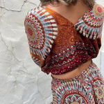 A woman wearing the orange Woven Floral Paisley Top and Trouser Set in font of a white wall.