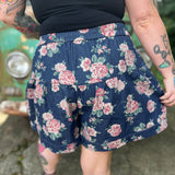 A woman wearing the Floral Print Denim Shorts in front of a teal vintage Volkswagen bus.