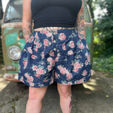 A woman wearing the Floral Print Denim Shorts in front of a teal vintage Volkswagen bus.