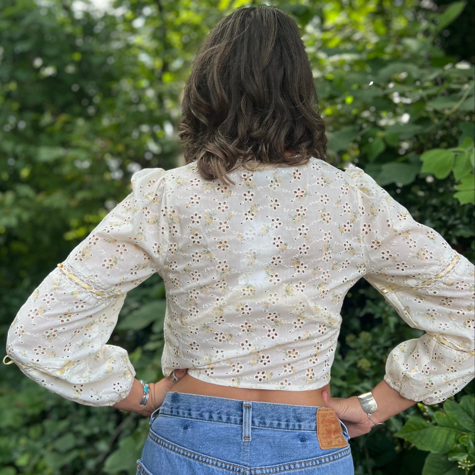A woman wearing the yellow Eyelet Floral Ribbon Trim Cotton Crop Top with jean shorts in front of some greenery.