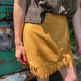 A woman wearing the Mustard Suede Fringe Wrap Skirt with a sparkly top.