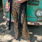 Someone wearing the Mustard Animal Print Bell Bottoms with Elastic Waist with a black fringe vest.