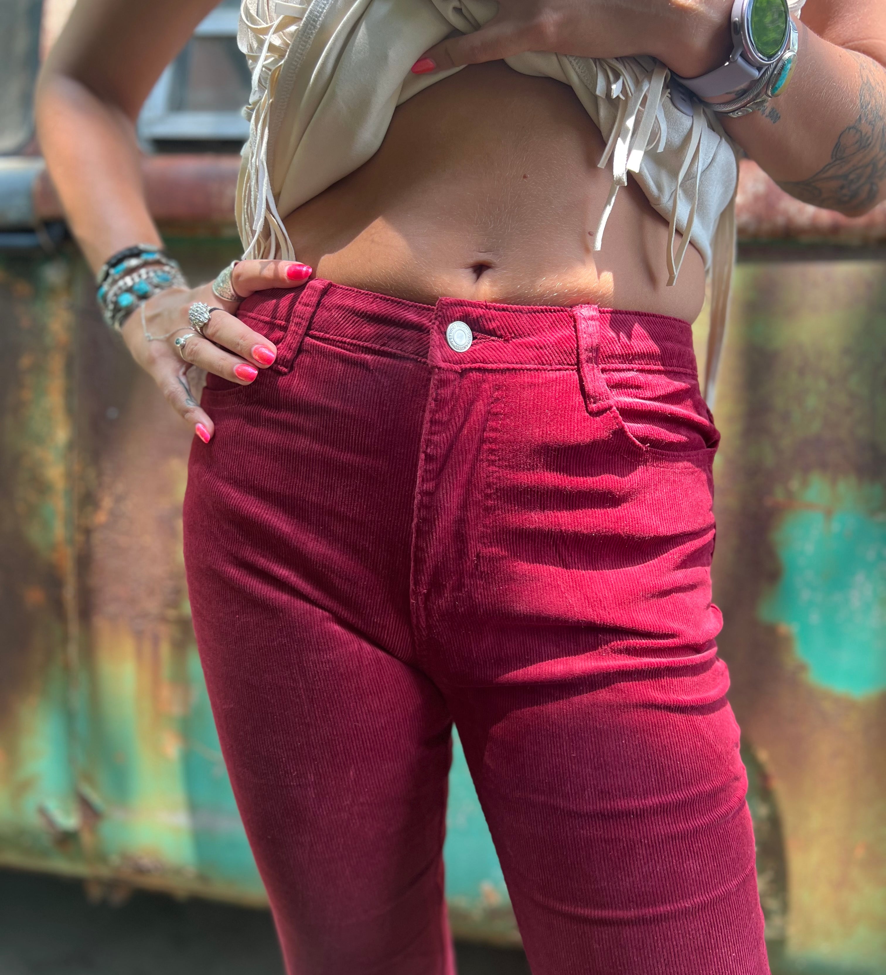 Someone wearing the Wine Soft Corduroy Flared Pants with Distressed Hem and a cream fringe top.