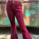 Someone wearing the Wine Soft Corduroy Flared Pants with Distressed Hem and a cream fringe top.