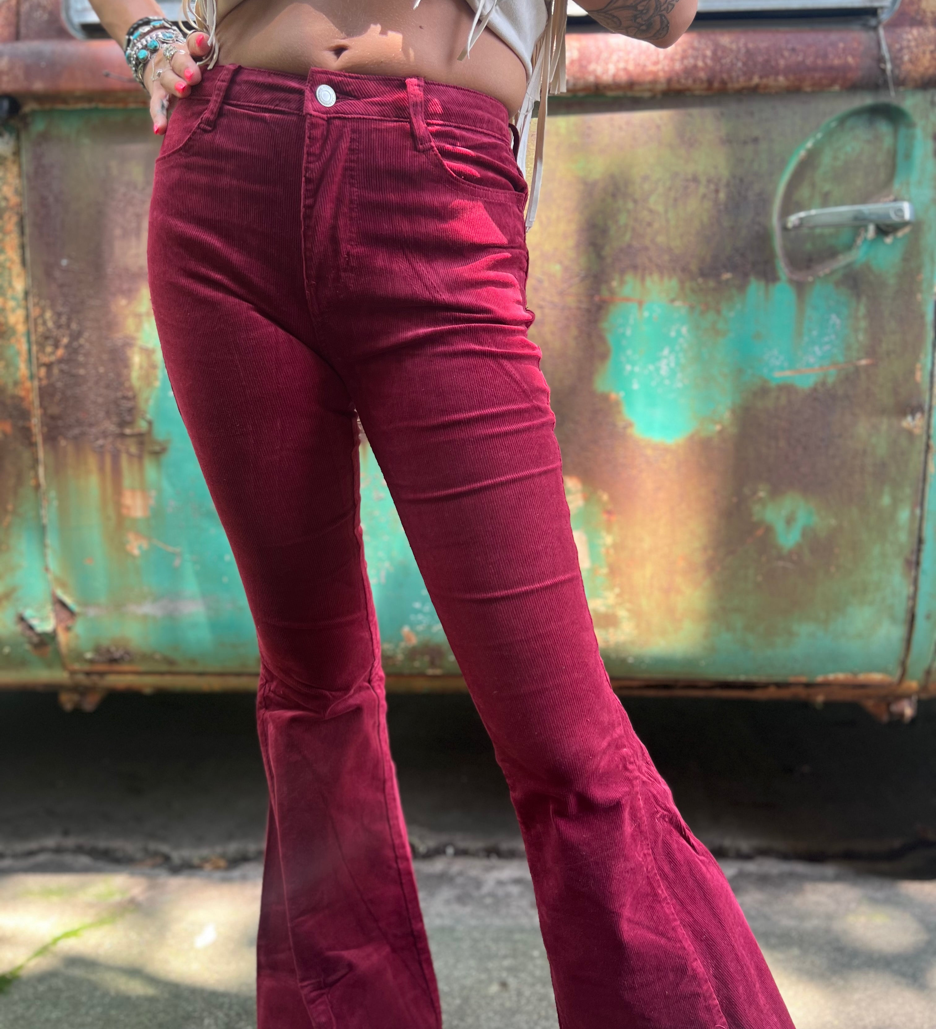 Someone wearing the Wine Soft Corduroy Flared Pants with Distressed Hem and a cream fringe top.