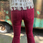 Someone wearing the Wine Soft Corduroy Flared Pants with Distressed Hem and a cream fringe top.