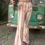 A woman wearing the Papaya Striped Washed Denim Bell Bottoms and a bralette while holding a bouquet.