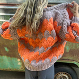 A woman wearing the Chunky Cardigan - Orange Taupe: One Size with a cream top and grey pants.