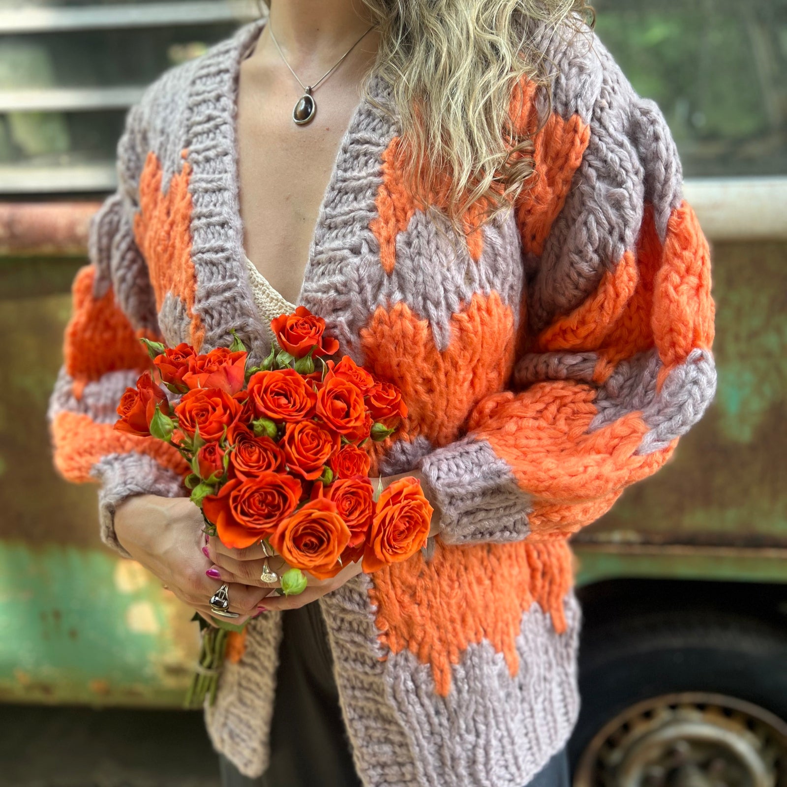 A woman wearing the Chunky Cardigan - Orange Taupe: One Size with a cream top and grey pants while holding a bouquet.