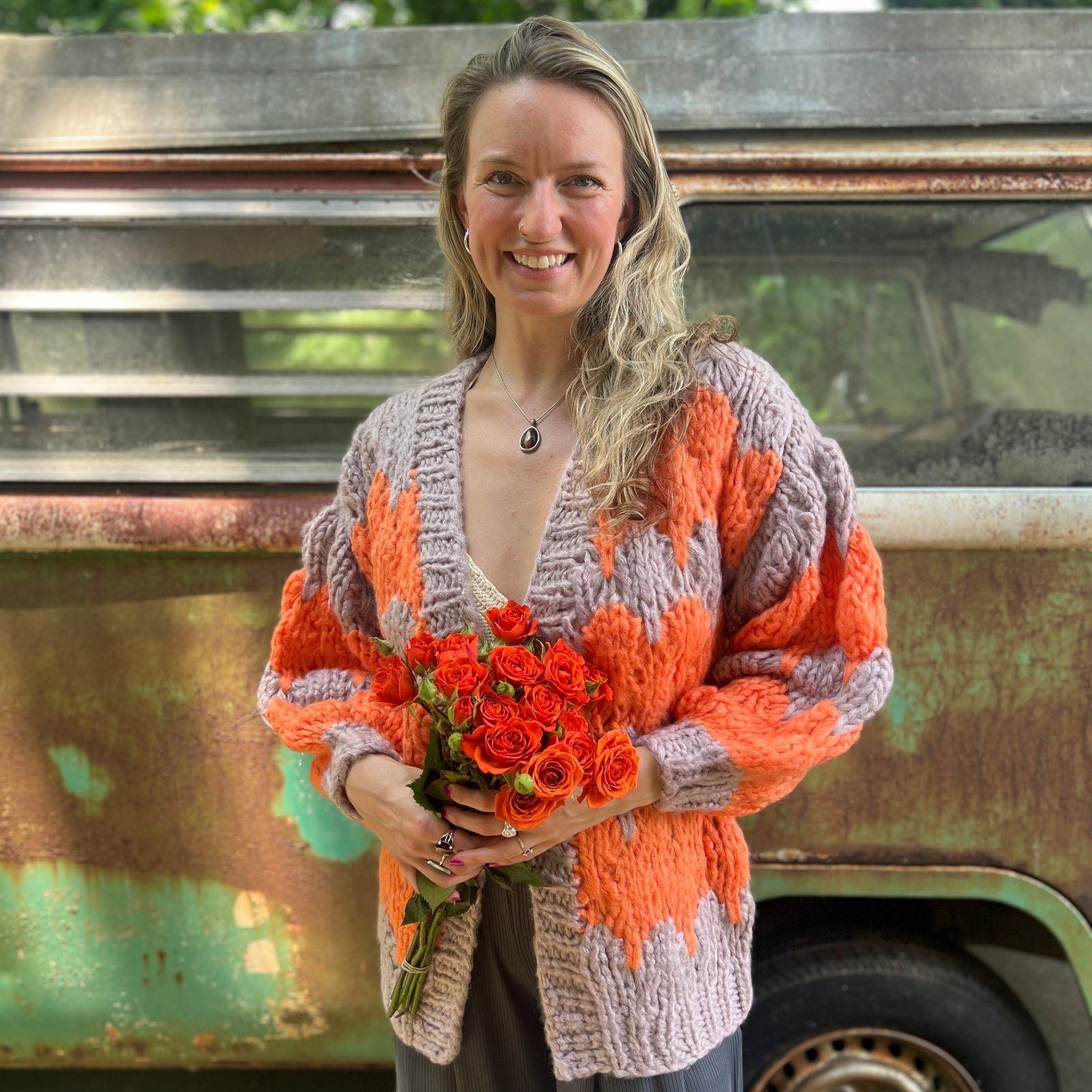 A woman wearing the Chunky Cardigan - Orange Taupe: One Size with a cream top and grey pants while holding a bouquet.