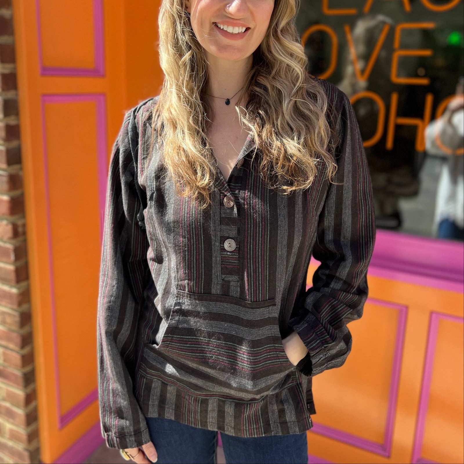 A woman wearing the agate Womens Half Button Baja Hoodie with jeans in front of a pink and orange wall.