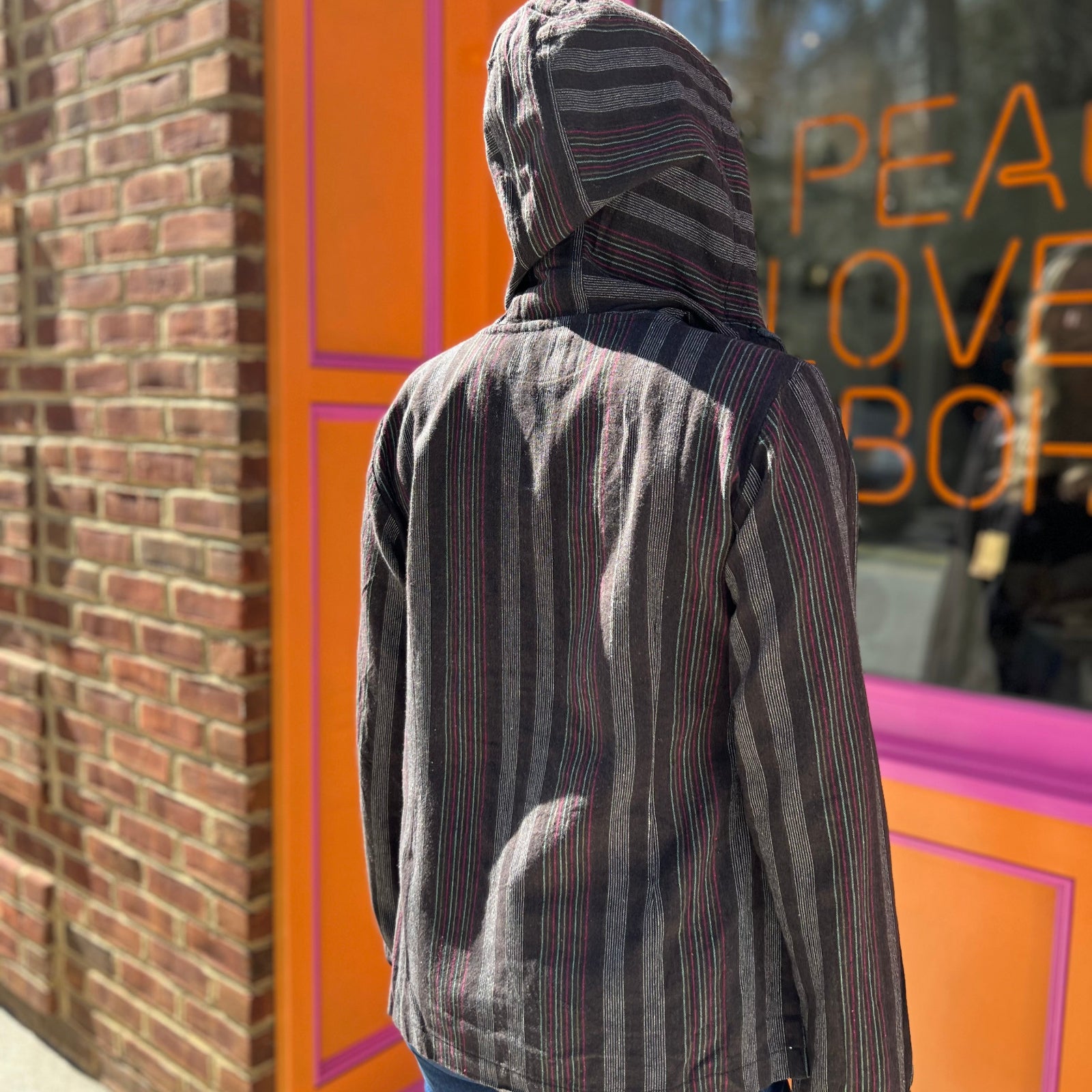 A woman wearing the agate Womens Half Button Baja Hoodie with jeans in front of a pink and orange wall.