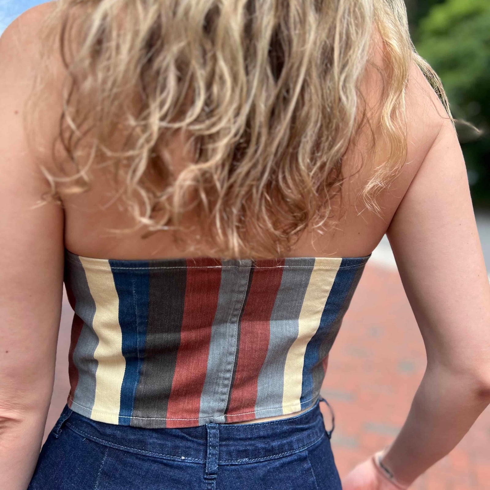 Back view of woman in striped tube top and high-waisted jeans showing textured blonde waves and boho hat