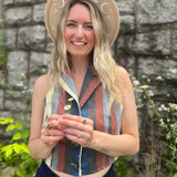 Woman in boho moon hat holding daisies, wearing a striped halter crop top and high-waisted jeans