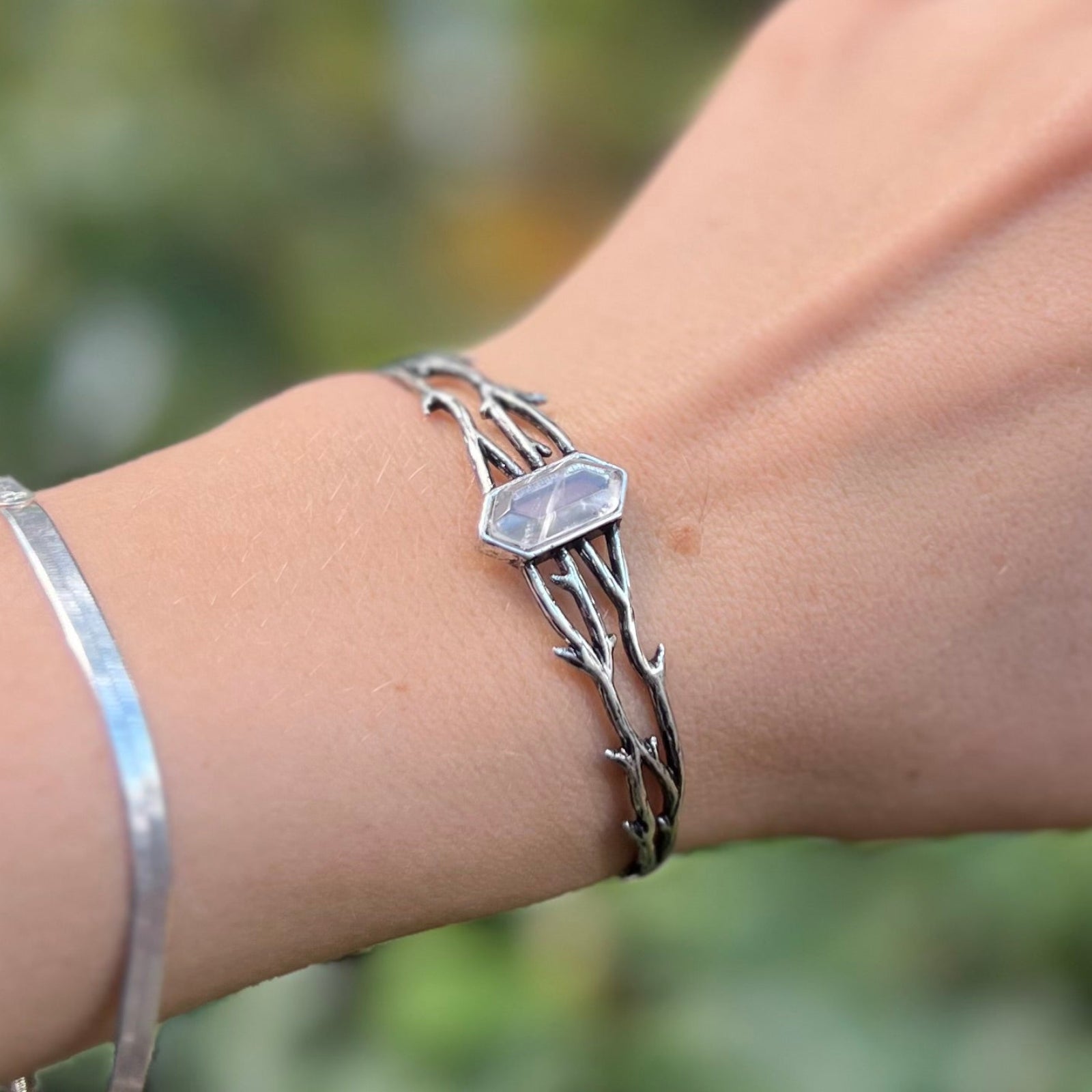 Someone wearing the Silver Thorn Cuff Bracelet in front of a green bush.