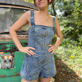 A woman wearing the medium wash Washed Western Buckle Embroidered Romper in front of a vintage teal Volkswagen bus.