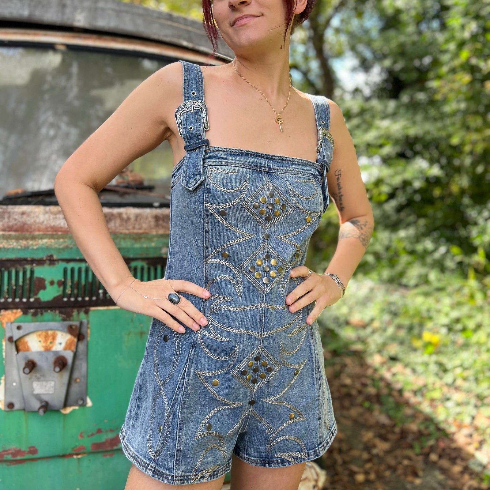 A woman wearing the medium wash Washed Western Buckle Embroidered Romper in front of a vintage teal Volkswagen bus.