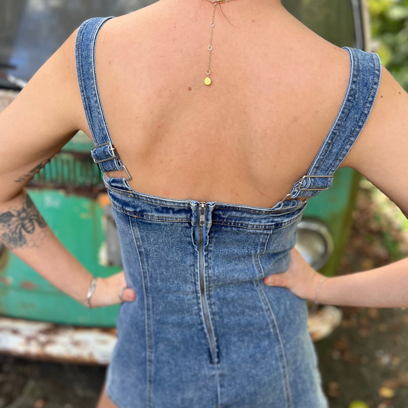 A woman wearing the medium wash Washed Western Buckle Embroidered Romper in front of a vintage teal Volkswagen bus.