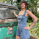A woman wearing the medium wash Washed Western Buckle Embroidered Romper in front of a vintage teal Volkswagen bus.