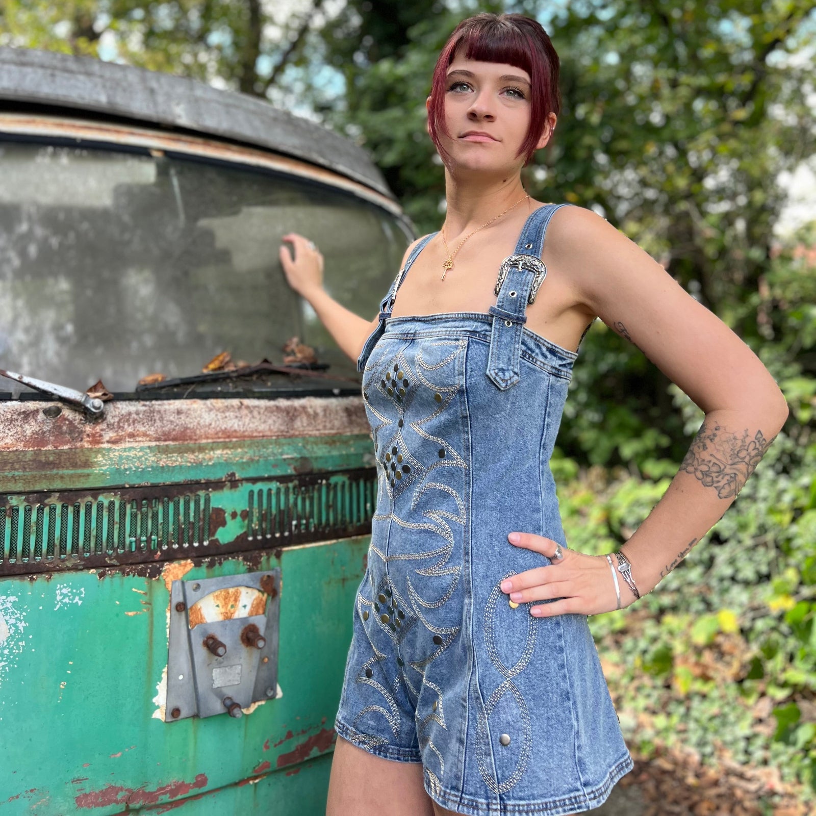 A woman wearing the medium wash Washed Western Buckle Embroidered Romper in front of a vintage teal Volkswagen bus.