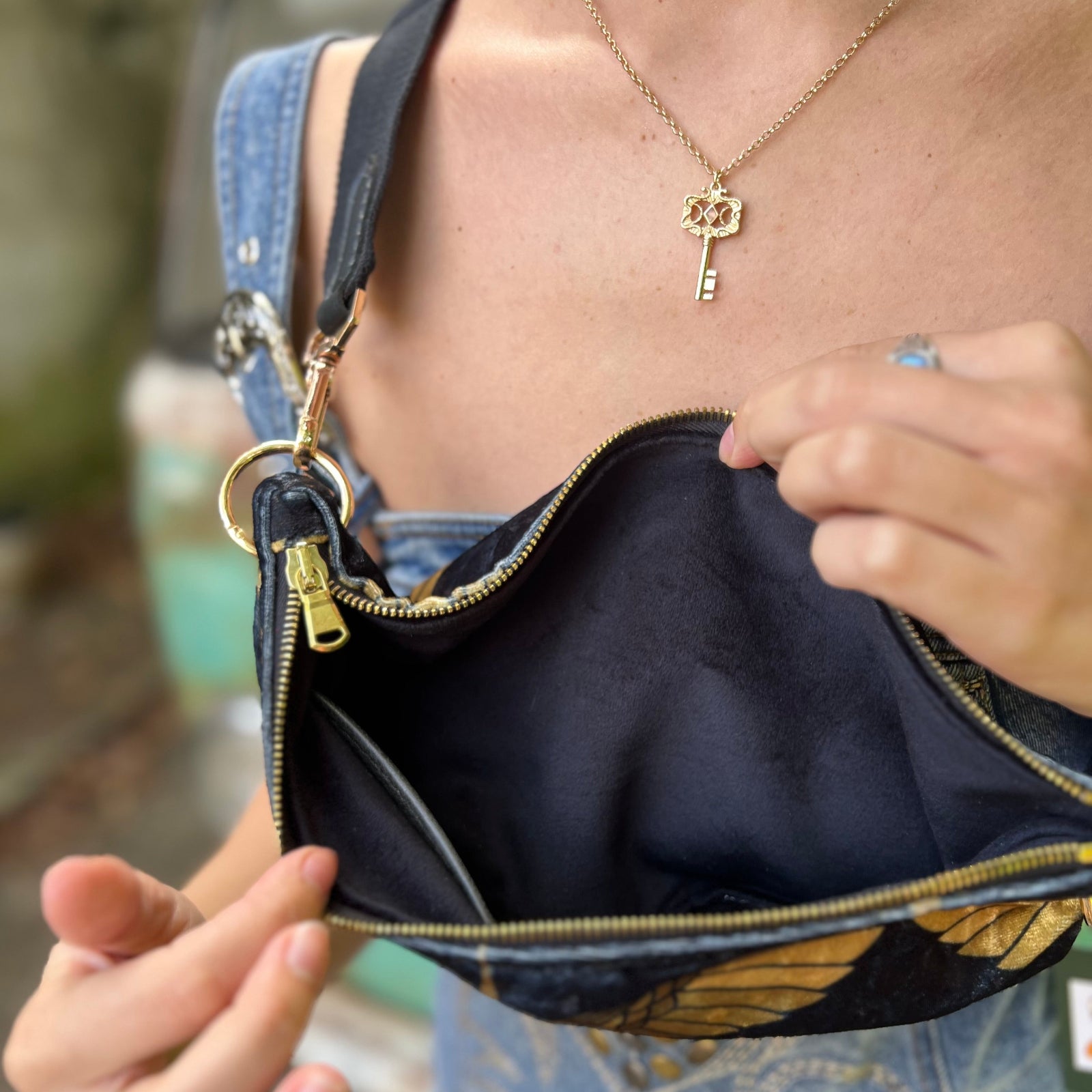 Someone wearing the Black And Gold Heron Fanny Bag with a denim romper, and holding the bag open.