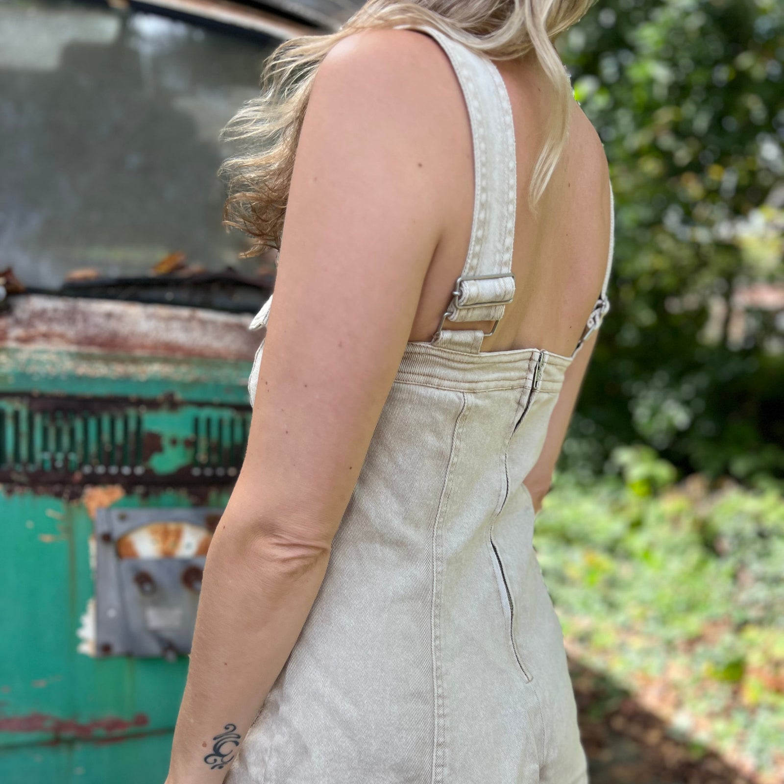 A woman wearing the sand Washed Western Buckle Embroidered Romper in front of a vintage teal Volkswagen bus.