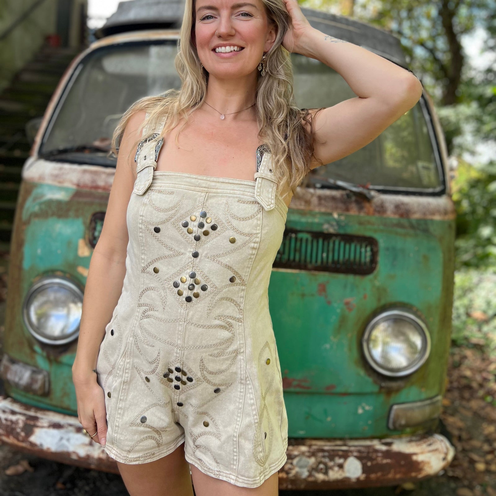 A woman wearing the sand Washed Western Buckle Embroidered Romper in front of a vintage teal Volkswagen bus.