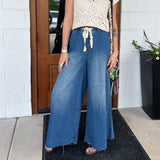 A woman wearing the dark wash Denim Drawstring Waist Band Wide Leg Pants with a cream crocheted top.