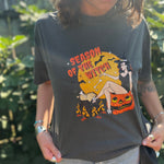 A woman wearing the Season Of The Witch Halloween Retro Cotton T-Shirt with jeans in front of some greenery.