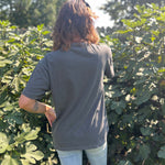 A woman wearing the Season Of The Witch Halloween Retro Cotton T-Shirt with jeans in front of some greenery, showing off the back.