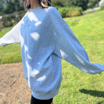 A woman wearing the Halloween Skeletons Gray Cotton Crewneck Sweatshirt with black shorts, showing off the side.