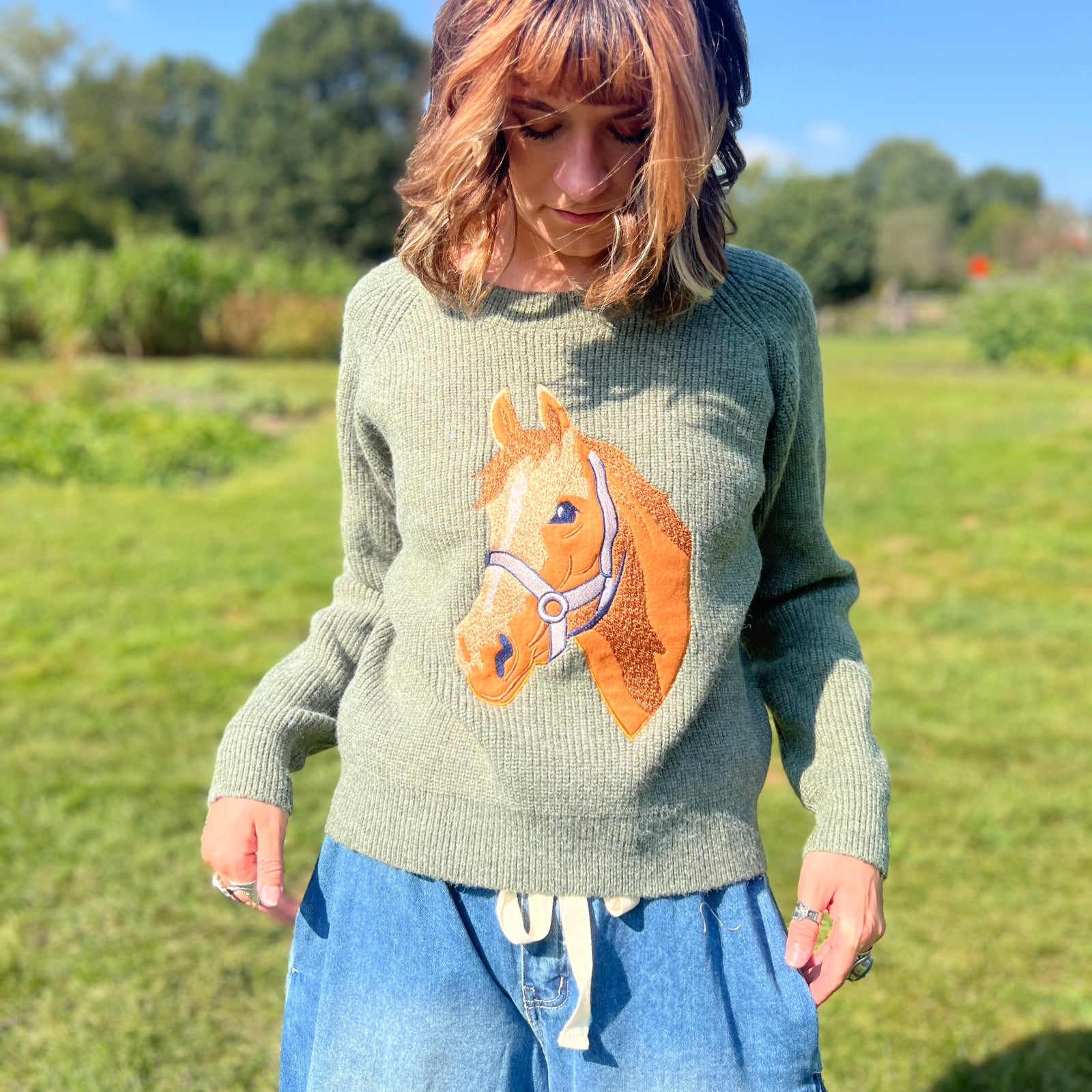 A woman wearing the Horse Embroidery Knit Pullover Sweater with the denim pants.