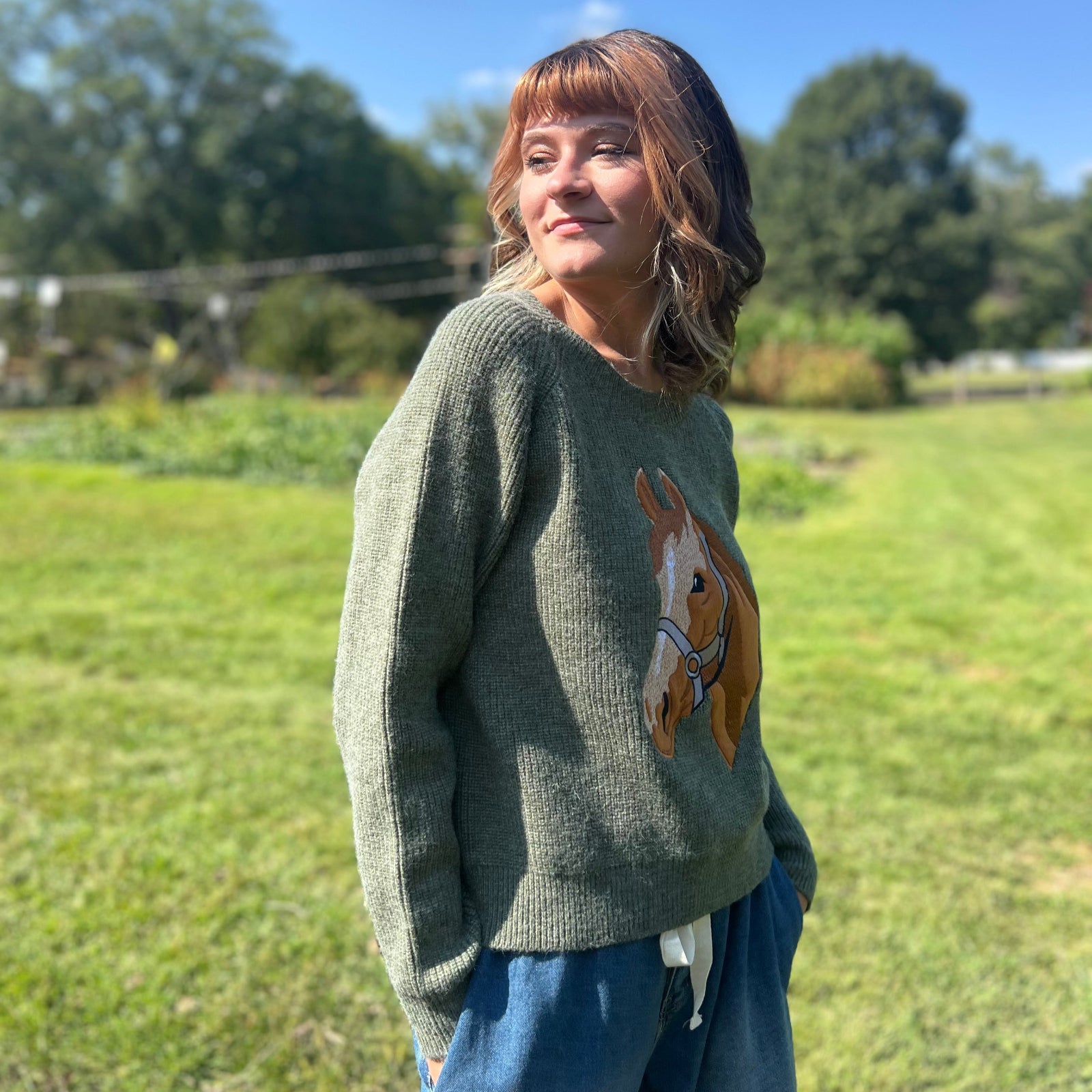 A woman wearing the Horse Embroidery Knit Pullover Sweater with the denim pants, showing off the side.
