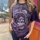 A woman wearing the Purple Mushroom Stonewashed Cotton T-shirt with jeans in front of a pink and orange wall.