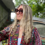 A woman wearing the turquoise Sofia Sunglasses with a colorful jacket.