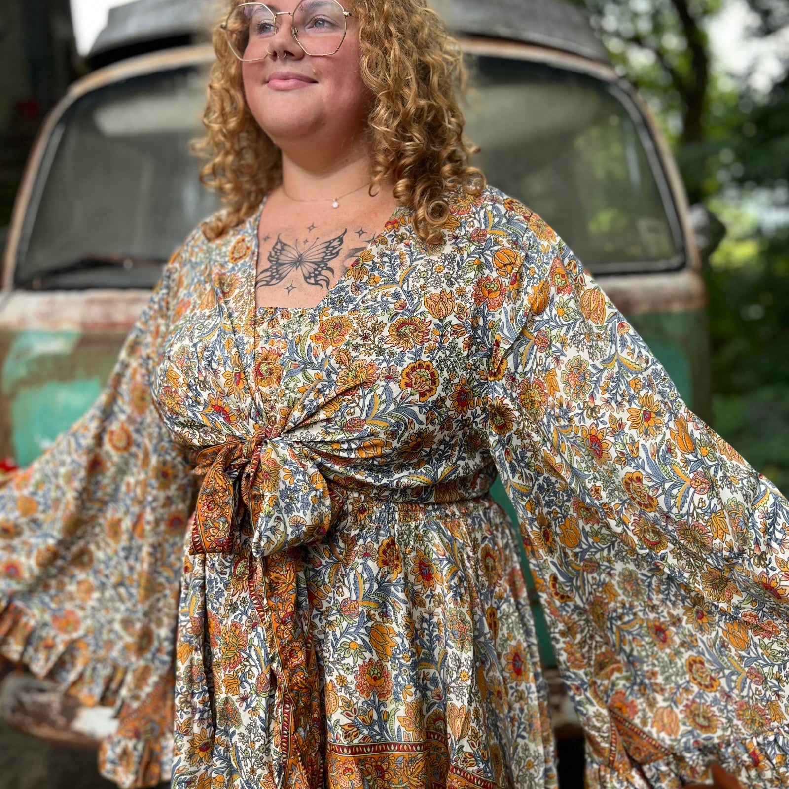 A woman wearing the orange and cream Hippie Bohemian Bell Sleeve Wrap Top with black pants in front of a rusted vintage Volkswagen bus.
