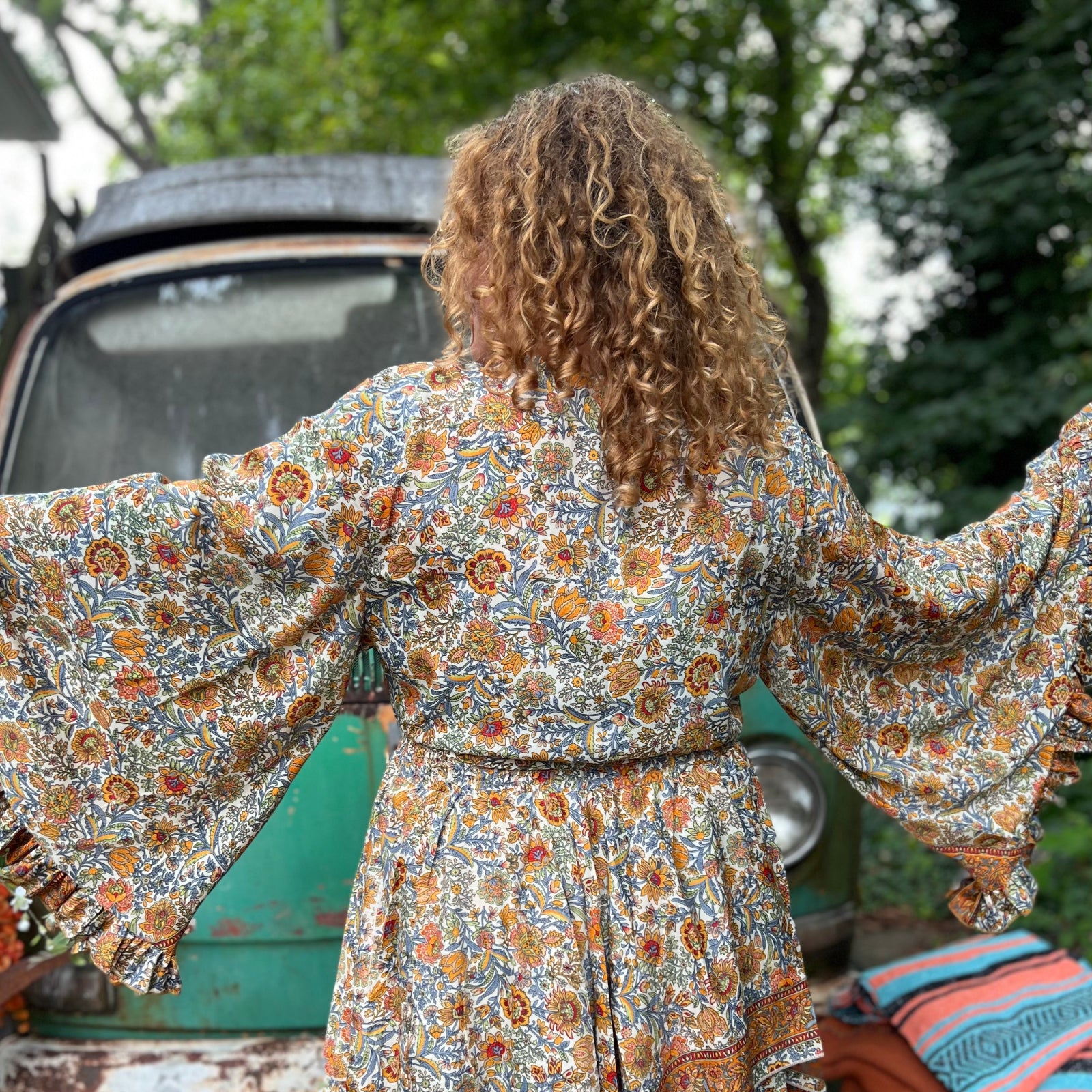 A woman wearing the orange and cream Hippie Bohemian Bell Sleeve Wrap Top with black pants in front of a rusted vintage Volkswagen bus.