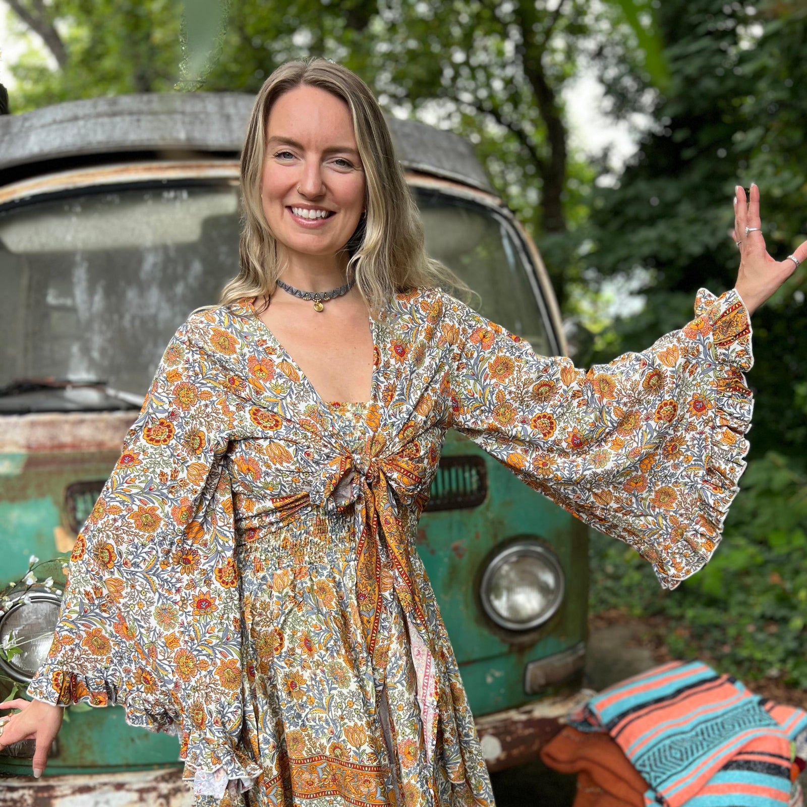 A woman wearing the orange and cream Hippie Bohemian Bell Sleeve Wrap Top with black pants in front of a rusted vintage Volkswagen bus.