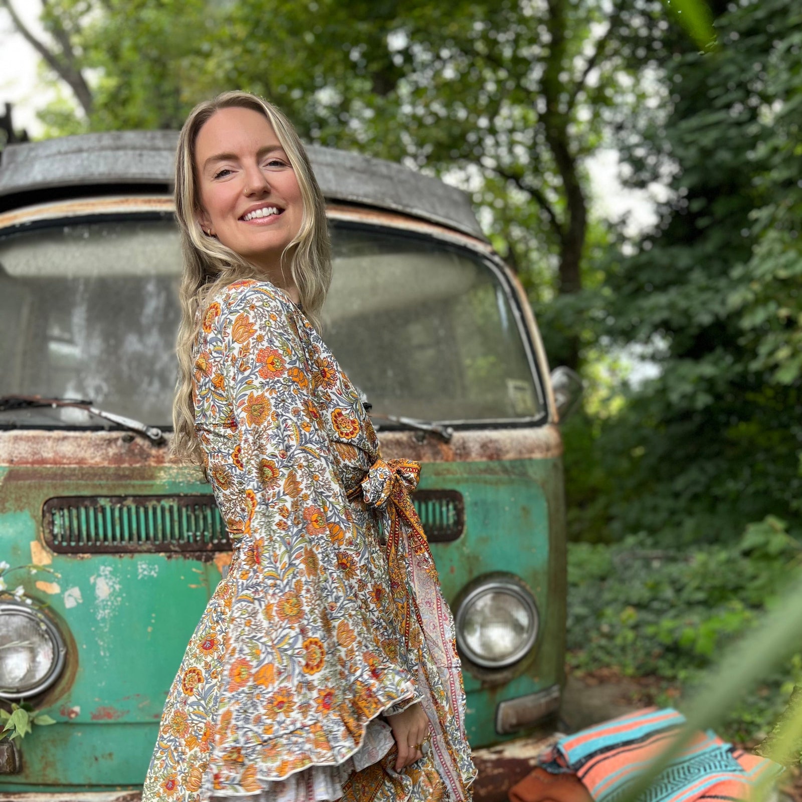 A woman wearing the orange and cream Hippie Bohemian Bell Sleeve Wrap Top with black pants in front of a rusted vintage Volkswagen bus.