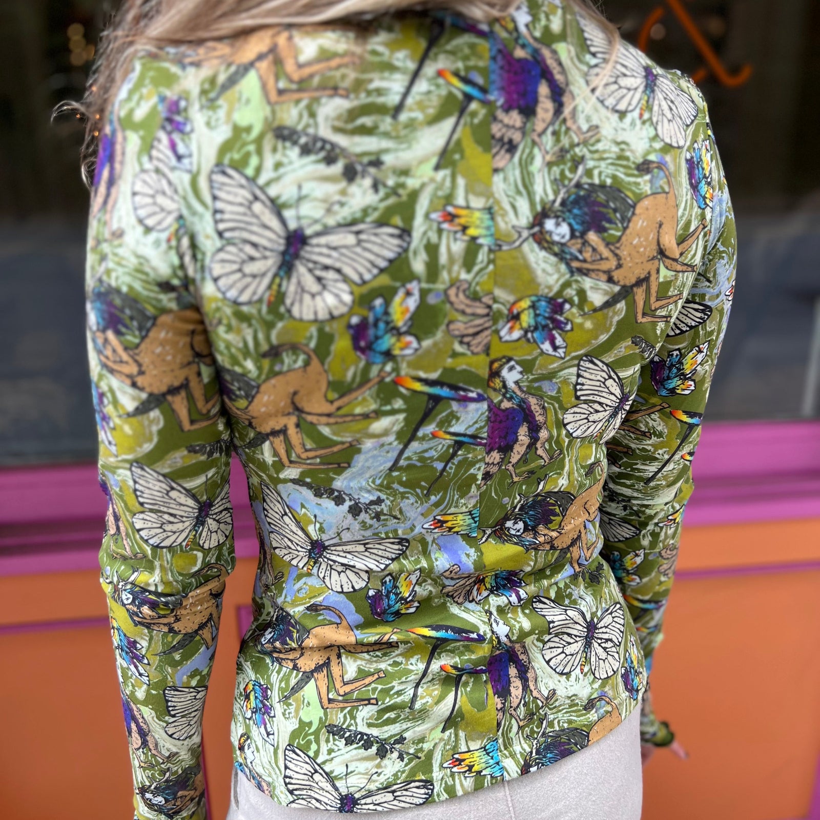 A woman wearing the green Cosmic Mythology Long Sleeve Top with beige linen pants in front of a window.