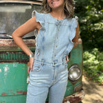 A woman wearing the Ruffle Button Up Bell Bottom Light Wash Denim Jumpsuit in front of a vintage teal Volkswagen bus.