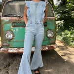 A woman wearing the Ruffle Button Up Bell Bottom Light Wash Denim Jumpsuit in front of a vintage teal Volkswagen bus.