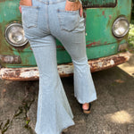 A woman wearing the Ruffle Button Up Bell Bottom Light Wash Denim Jumpsuit in front of a vintage teal Volkswagen bus.