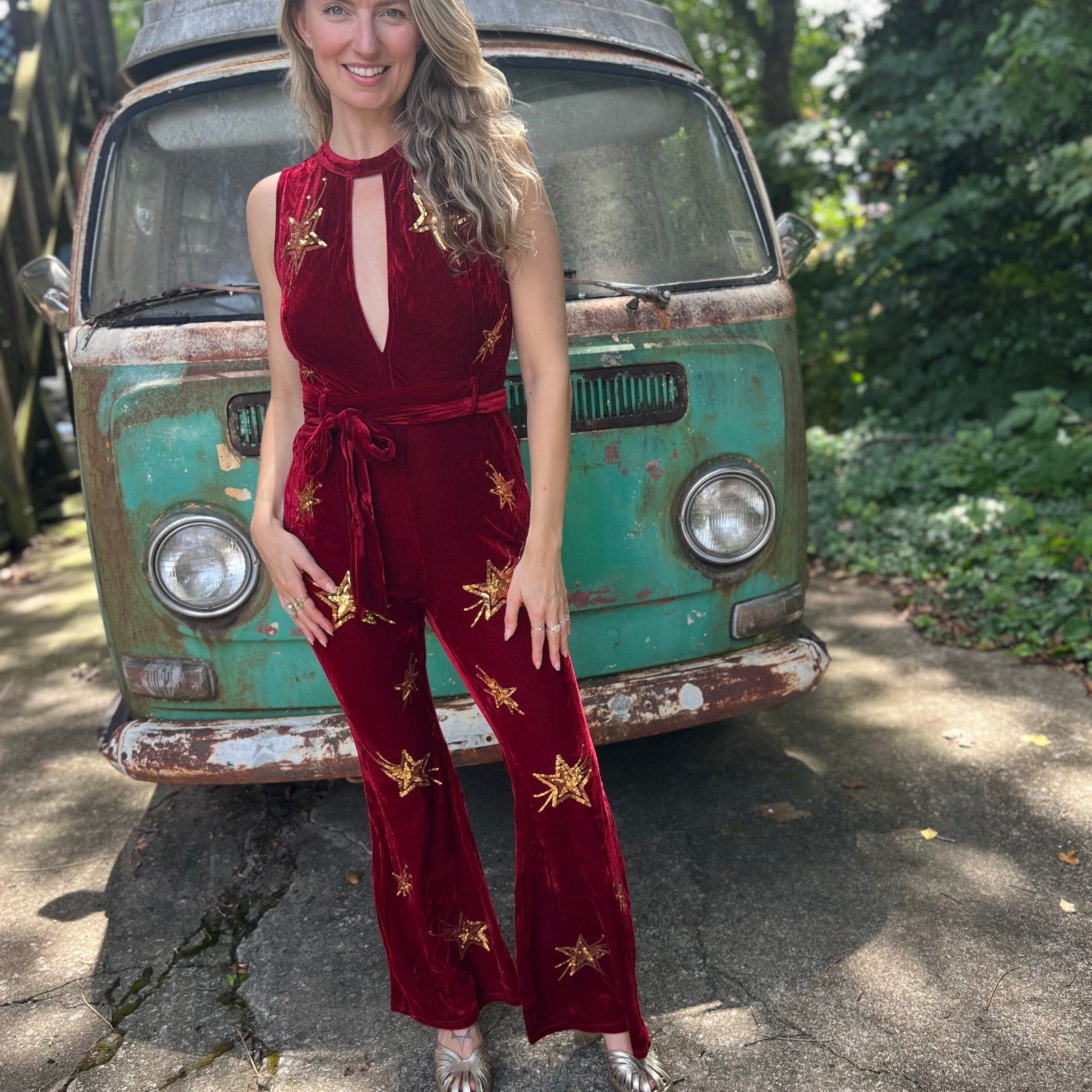 A woman wearing the burgundy Suede Sequin Embellished Embroidered Bootcut Jumpsuit in front of a teal vintage Volkswagen bus.