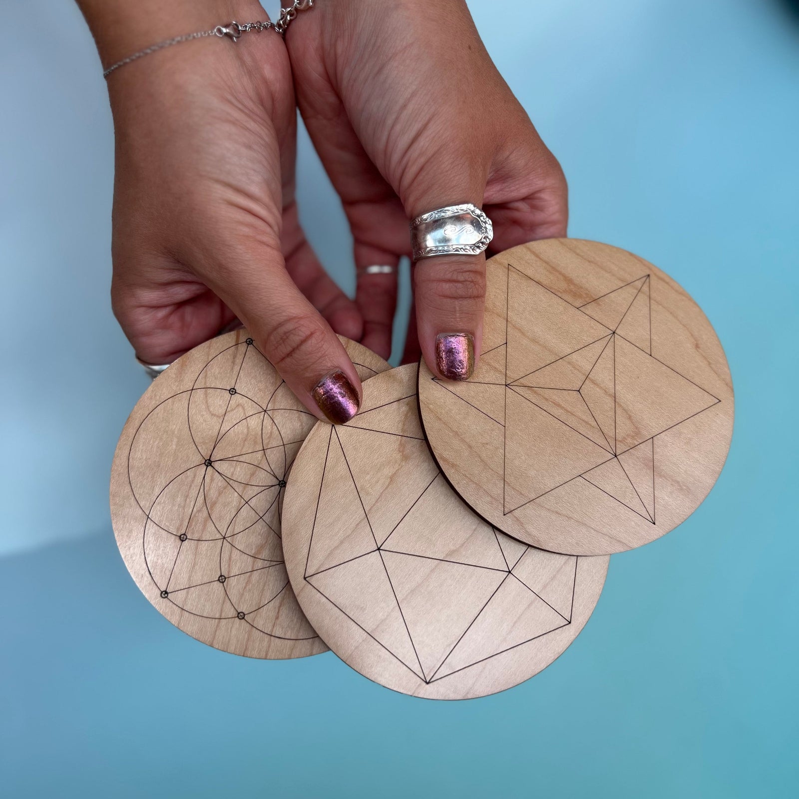 Someone holding three wooden crystal grids in front of a light blue background.