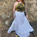 A woman wearing a tie dye top with the white Homespun Tiered Maxi Skirt in front of a rock wall.