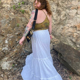 A woman wearing a tie dye top with the white Homespun Tiered Maxi Skirt in front of a rock wall.
