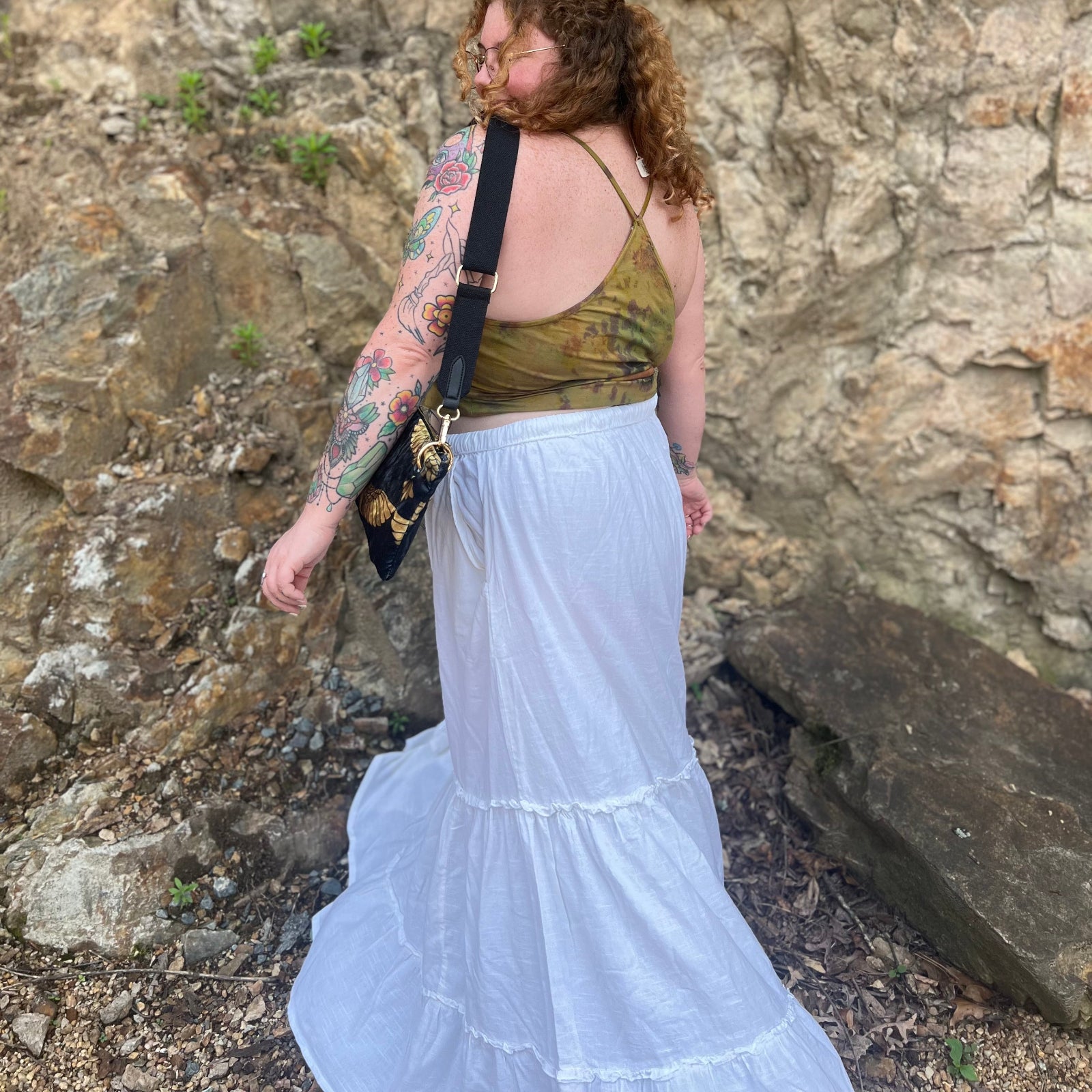 A woman wearing a tie dye top with the white Homespun Tiered Maxi Skirt in front of a rock wall.