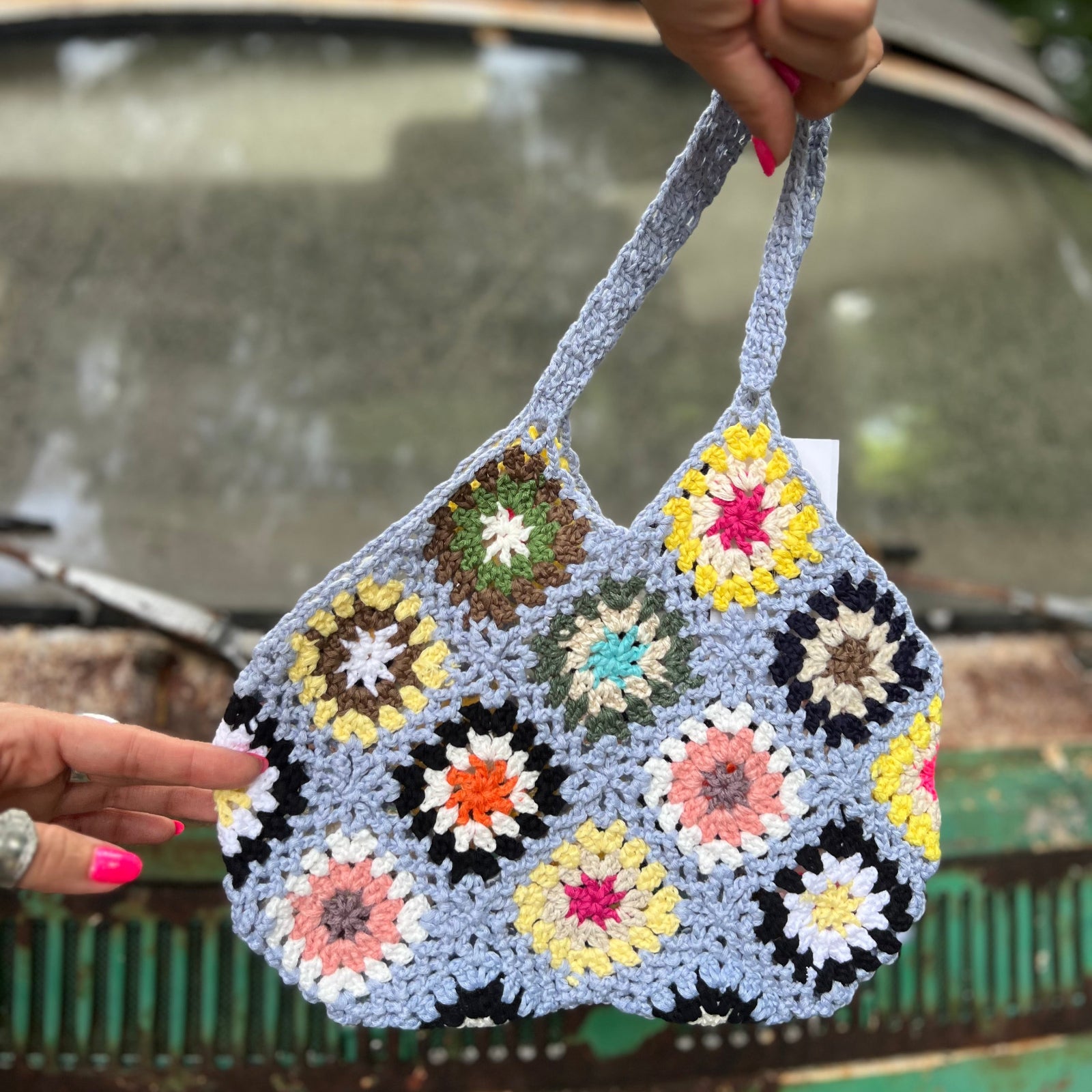 Someone holding the blue Bohemian Handmade Crochet Bag in front of a teal Volkswagen bus.