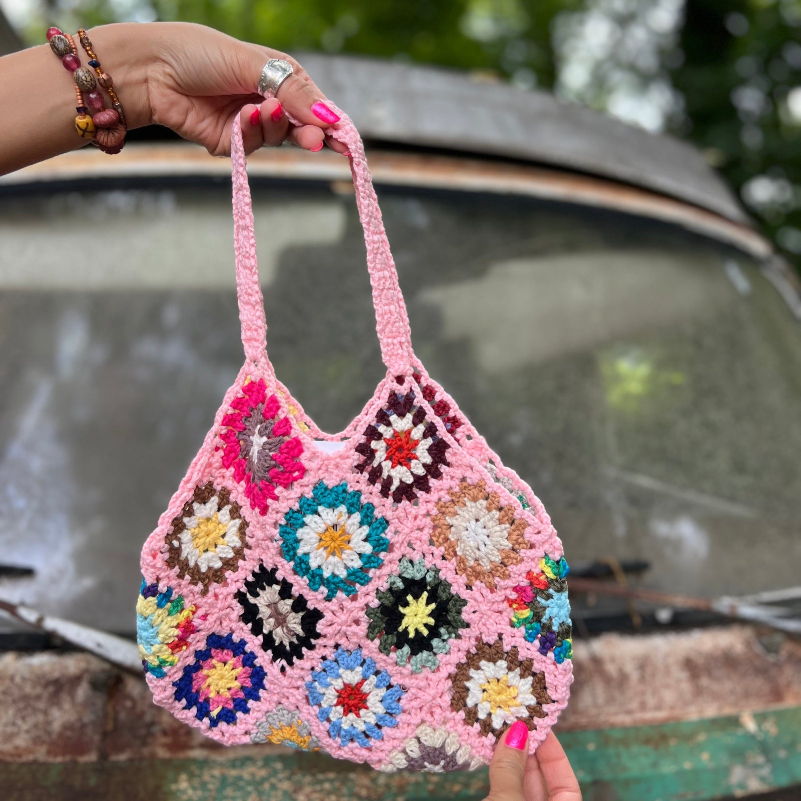 Someone holding the pink Bohemian Handmade Crochet Bag in front of an old teal Volkswagen bus.
